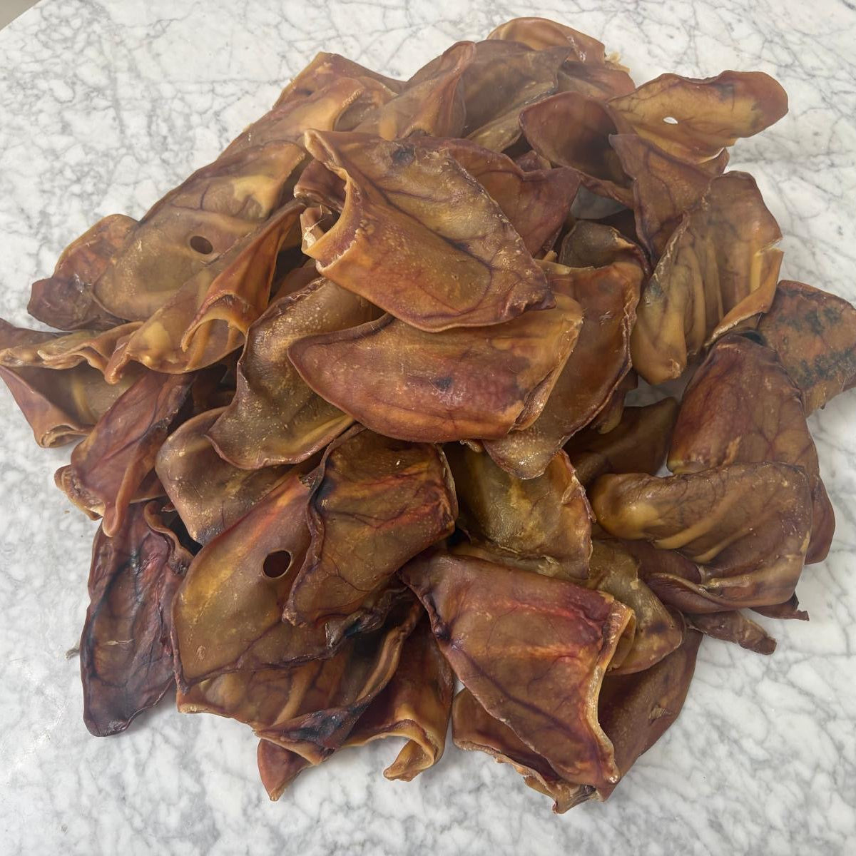 Stack of natural dried pigs ear dog treats on a marble surface
